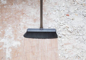 Broom sweeping concrete pieces from floor. Cleaning garbage after repair work of home. Closeup.